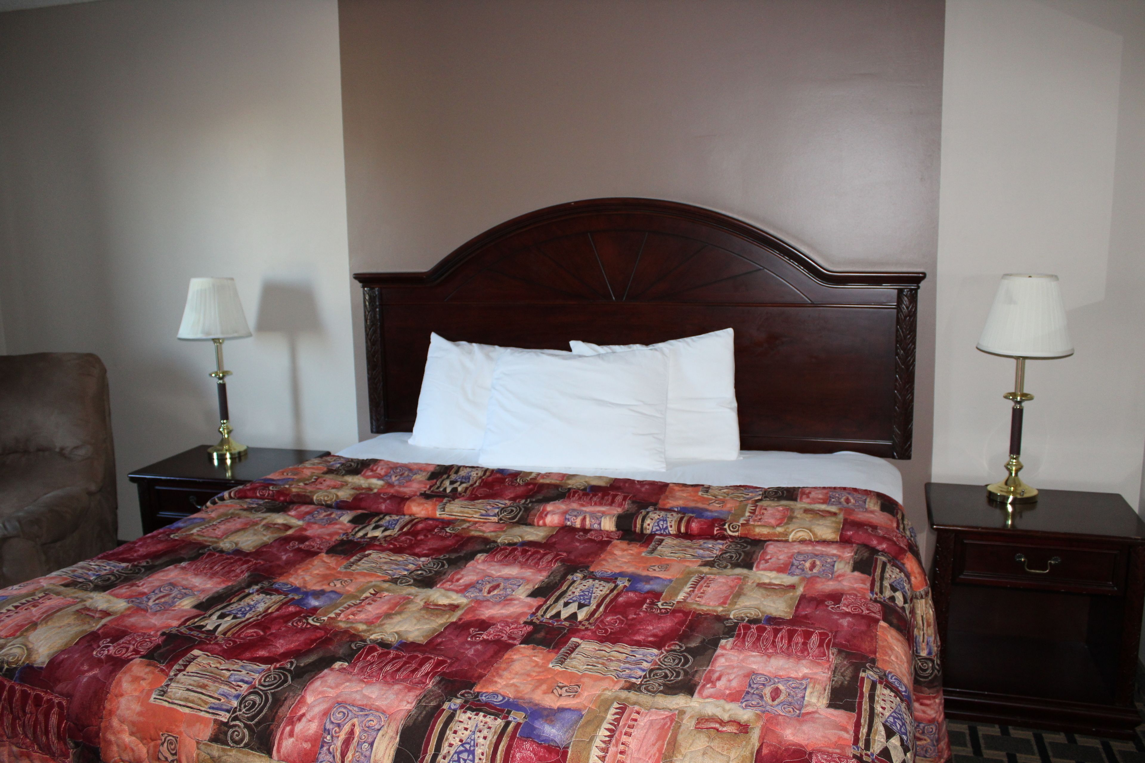 Una cama bien hecha con un edredón estampado, dos mesitas de noche con lámparas y una silla.