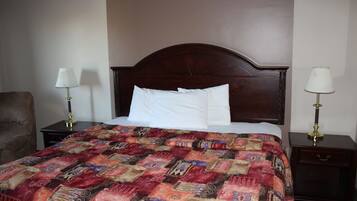 Una cama bien hecha con un edredón estampado, dos mesitas de noche con lámparas y una silla.