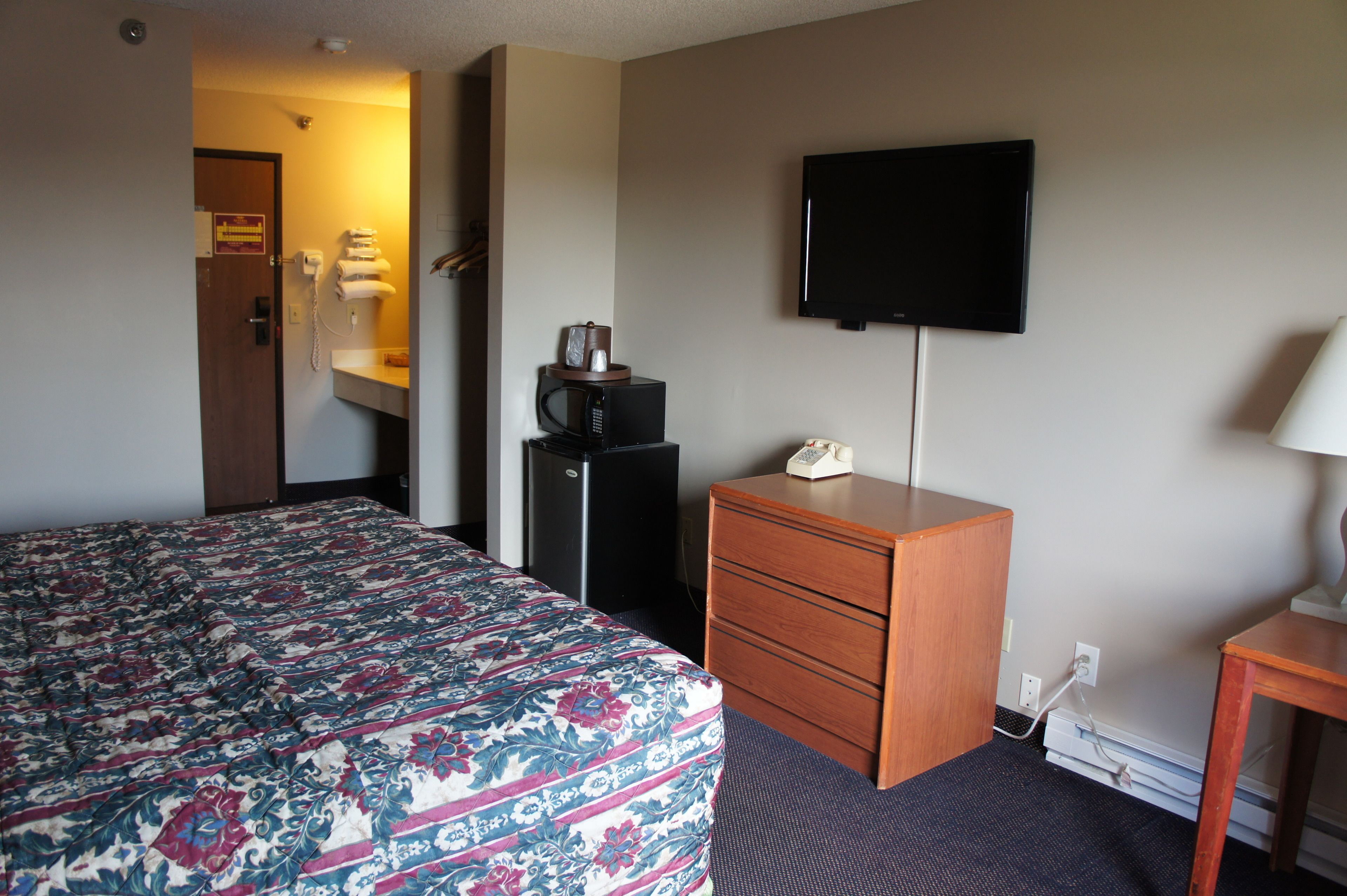 A hotel room with a bed, a desk, a television, a microwave, and a telephone.
