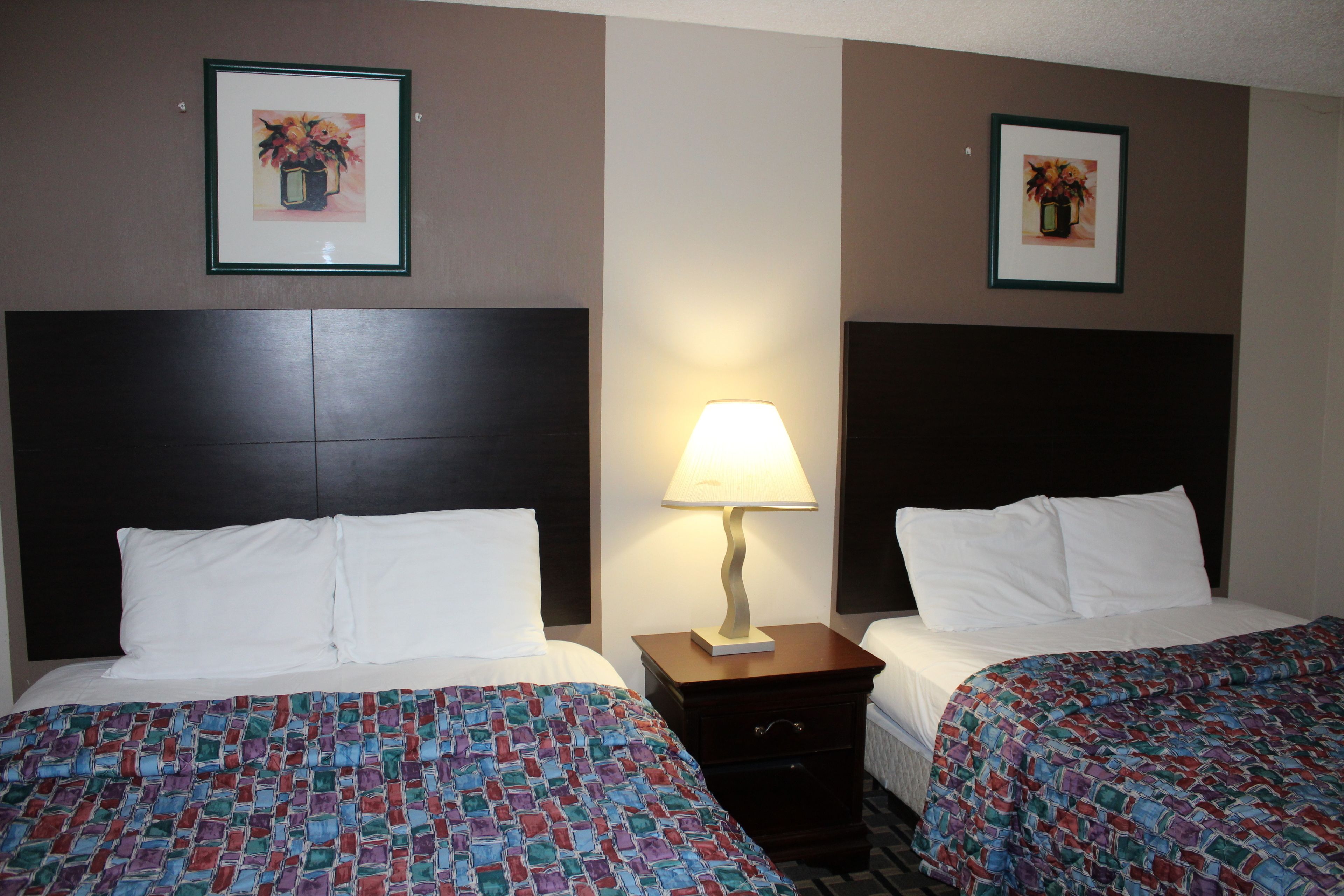 A hotel room with two beds, a nightstand with a lamp, and framed artwork on the walls.