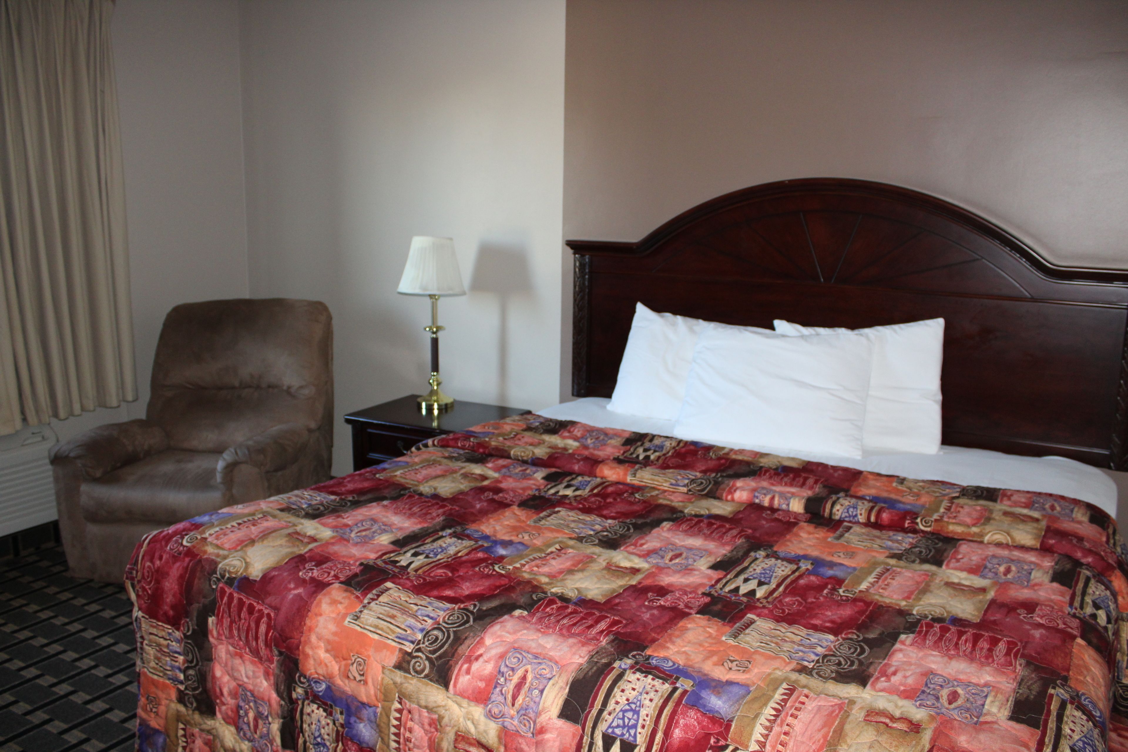 A hotel room with a large bed, a chair, a nightstand, and a lamp.