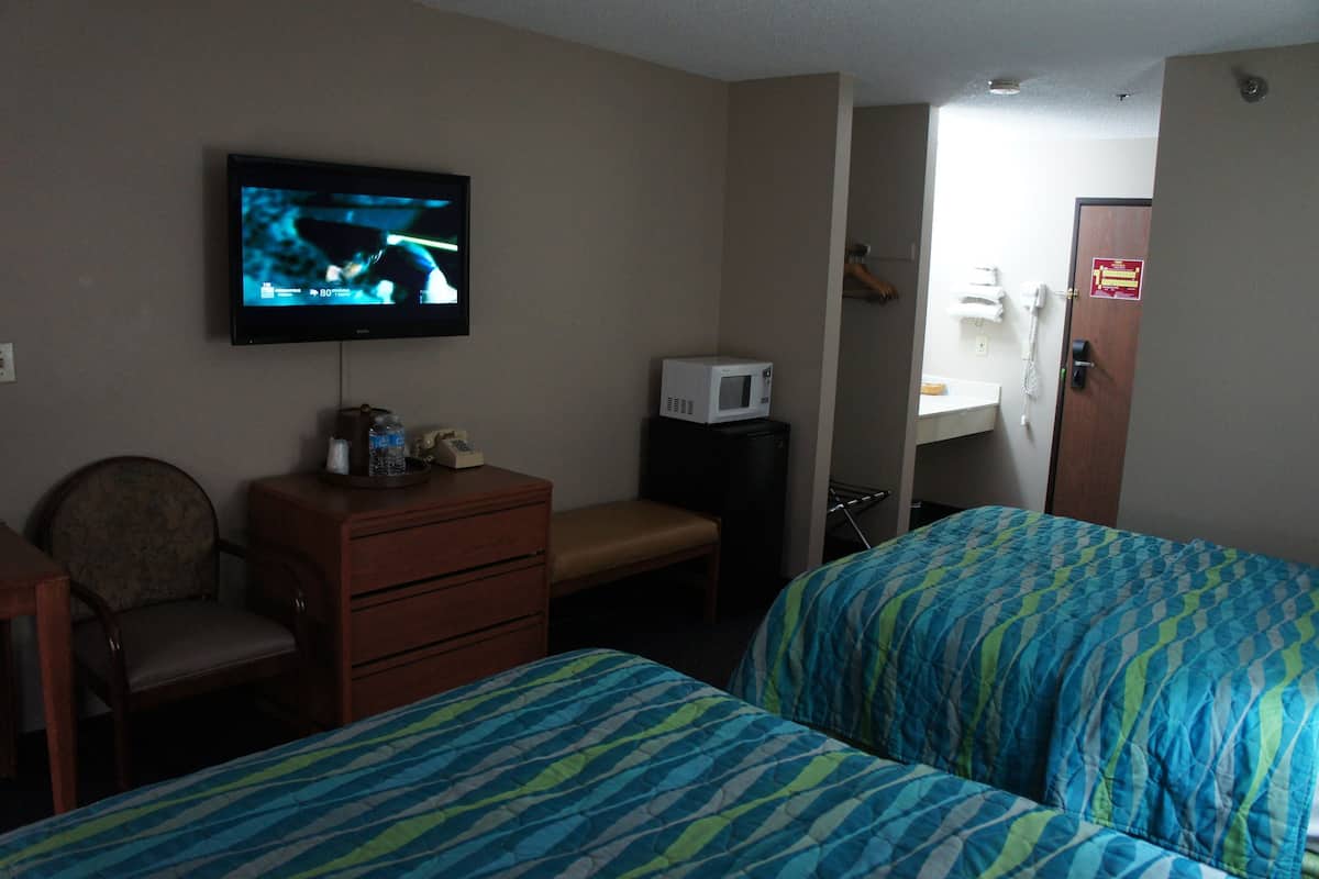 Quarto de hotel com duas camas, televisão, micro-ondas, secretária e uma cadeira.