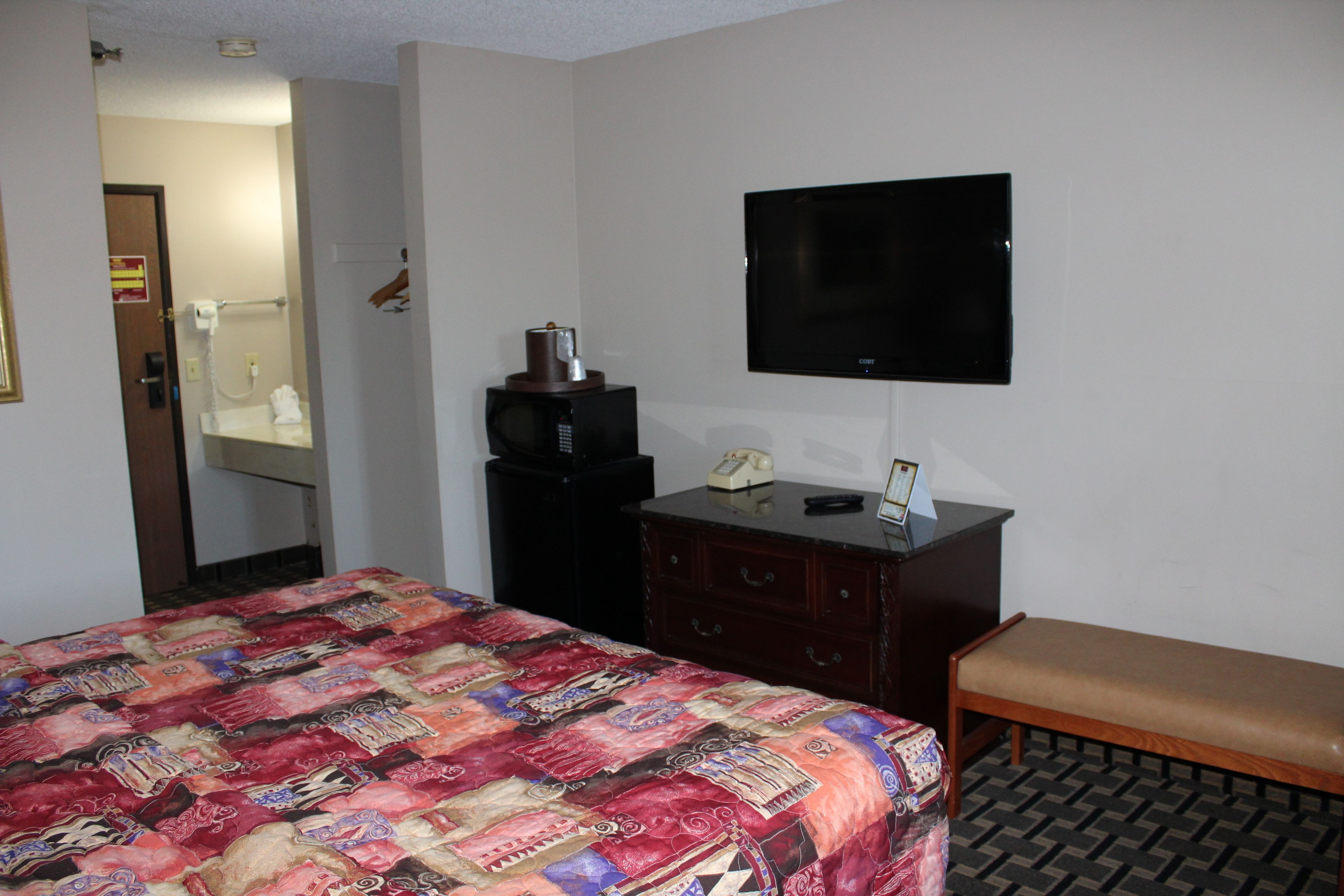 A hotel room with a bed, a wooden bench, a dresser, a television, and a mirror.