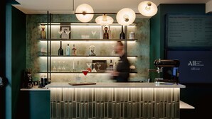Zona de bar con barra, estantes con botellas, vasos y una pizarra de menú.