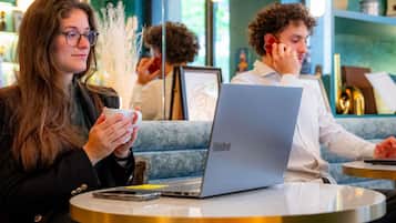 A person sitting at a round table with a laptop, holding a cup.