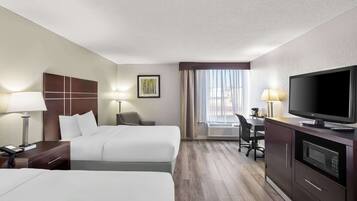 A hotel room with two beds, a desk with a chair, a television, a microwave, and a window with curtains.