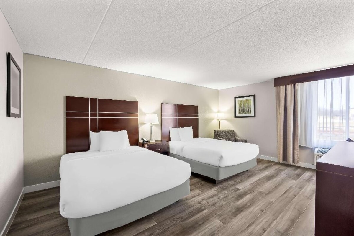 A hotel room with two beds, a desk, and a window with curtains.