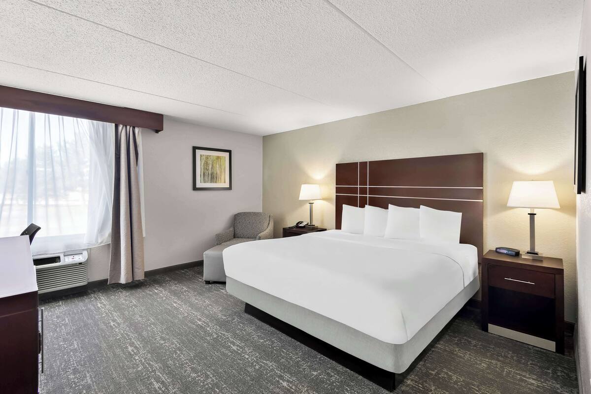 Une chambre d’hôtel avec un grand lit, deux tables de chevet avec des lampes, une chaise et une fenêtre avec des rideaux.