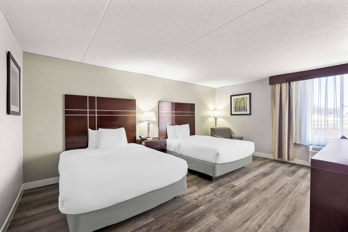 Une chambre d’hôtel avec deux lits, un bureau et une fenêtre avec des rideaux.
