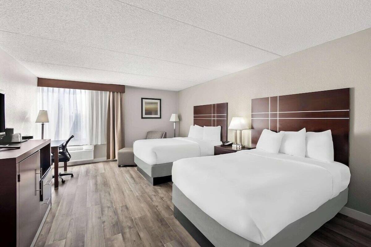 A hotel room with two beds, a desk, a chair, a TV, and a window with curtains.