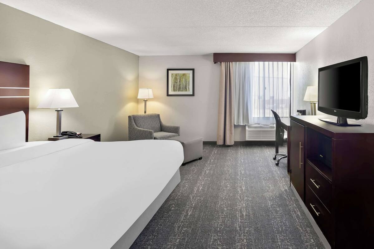 Une chambre d’hôtel avec un grand lit, un bureau, une chaise, une télévision et une fenêtre avec des rideaux.
