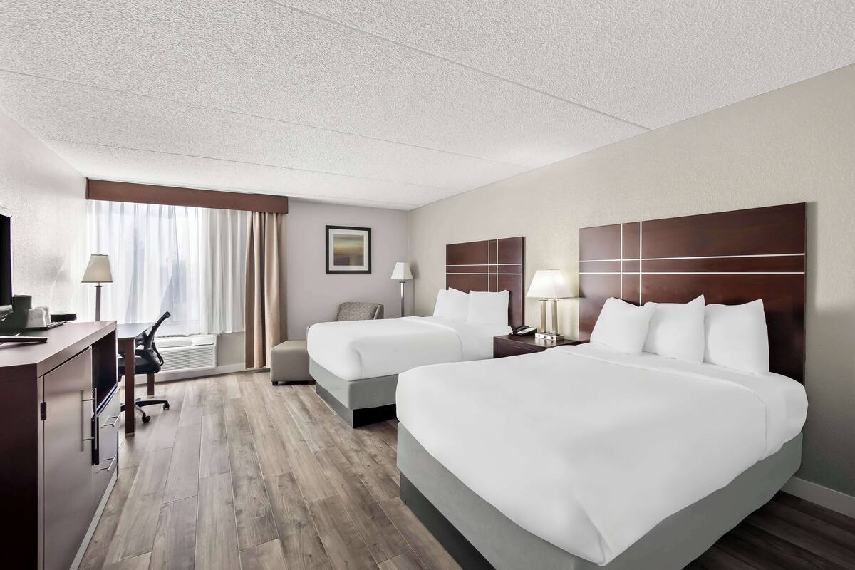 Une chambre d’hôtel avec deux lits, un bureau, une chaise et une fenêtre avec des rideaux.