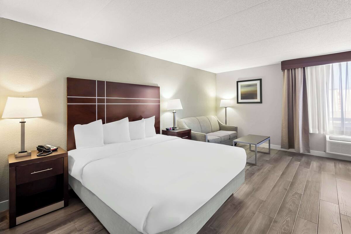 Une chambre d’hôtel avec un grand lit, deux tables de chevet avec des lampes, un petit canapé et une fenêtre avec des rideaux.