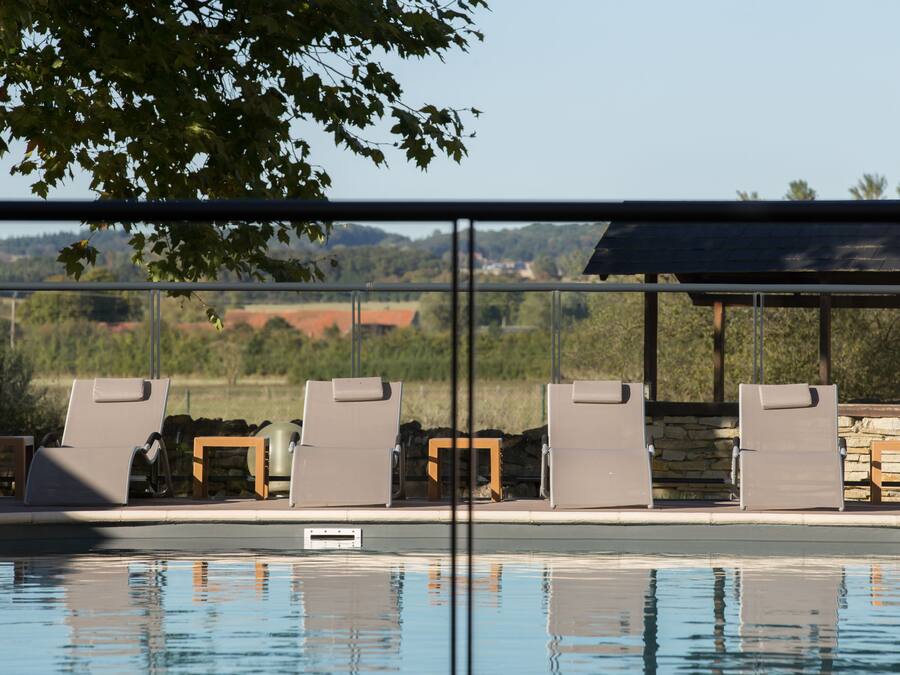 Zona de piscina con sillones de descanso y pared de piedra.