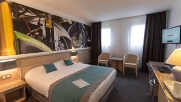 Quarto de hotel com uma cama grande, uma escrivaninha com um laptop, uma cadeira e uma televisão exibindo "WELCOME".