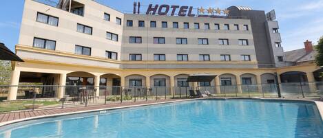 A hotel with a swimming pool, outdoor seating, and a clear sky.