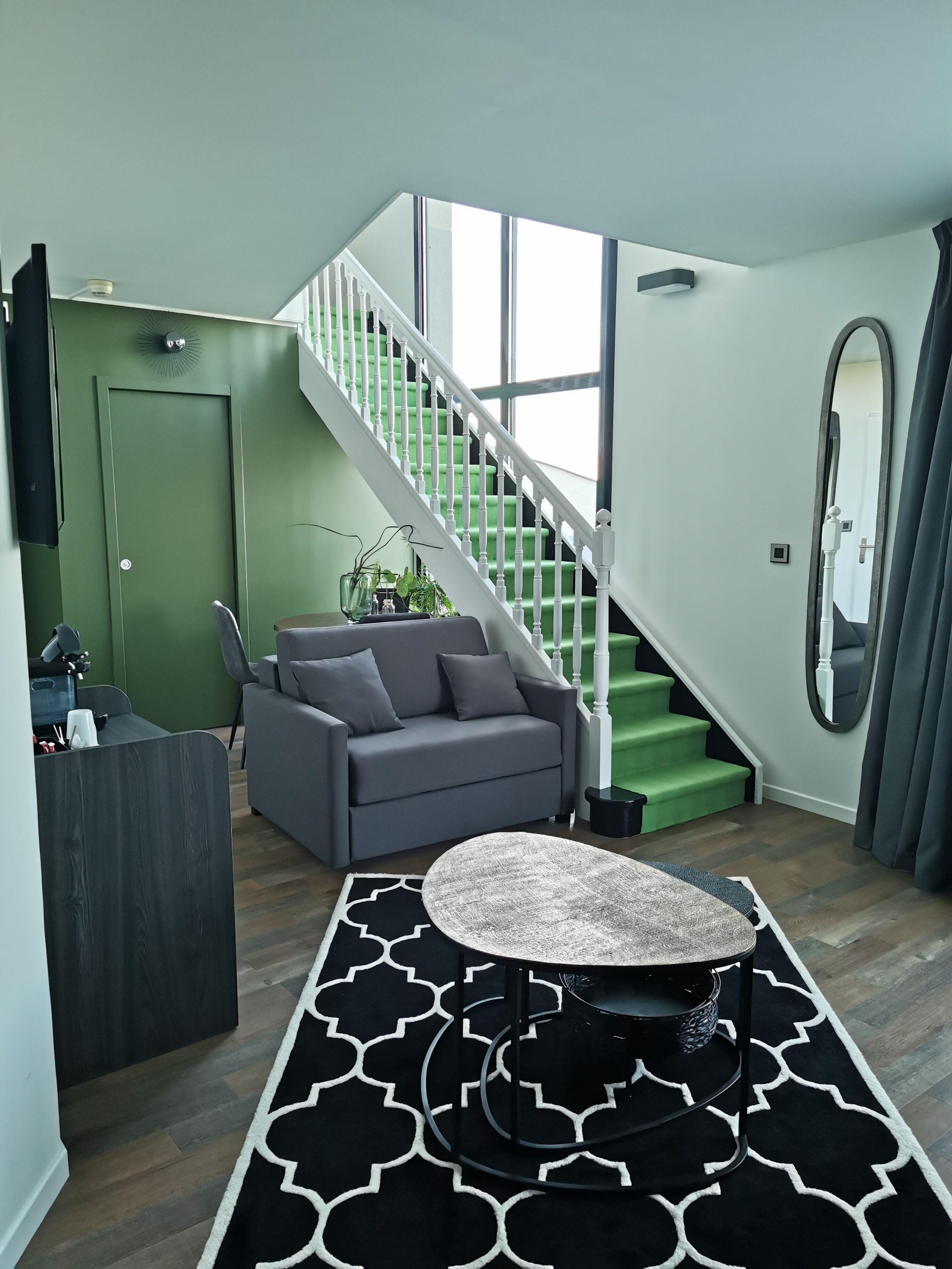 Uma sala de estar moderna com um sofá cinza, uma mesa de centro redonda e uma escada com degraus verdes.