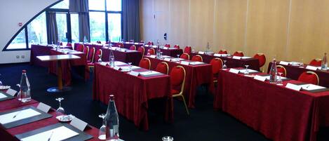 A conference room with multiple tables, red chairs, and tables set with water bottles, glasses, and nameplates.