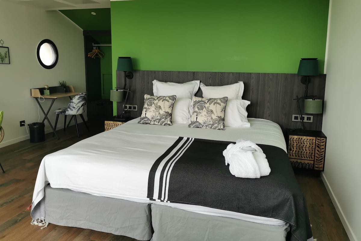 A modern hotel room with a large bed, a desk, and a green accent wall.