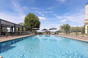 A swimming pool with lounge chairs and umbrellas, surrounded by a fence and trees. - Hôtel Le Paddock (Magny-Cours)