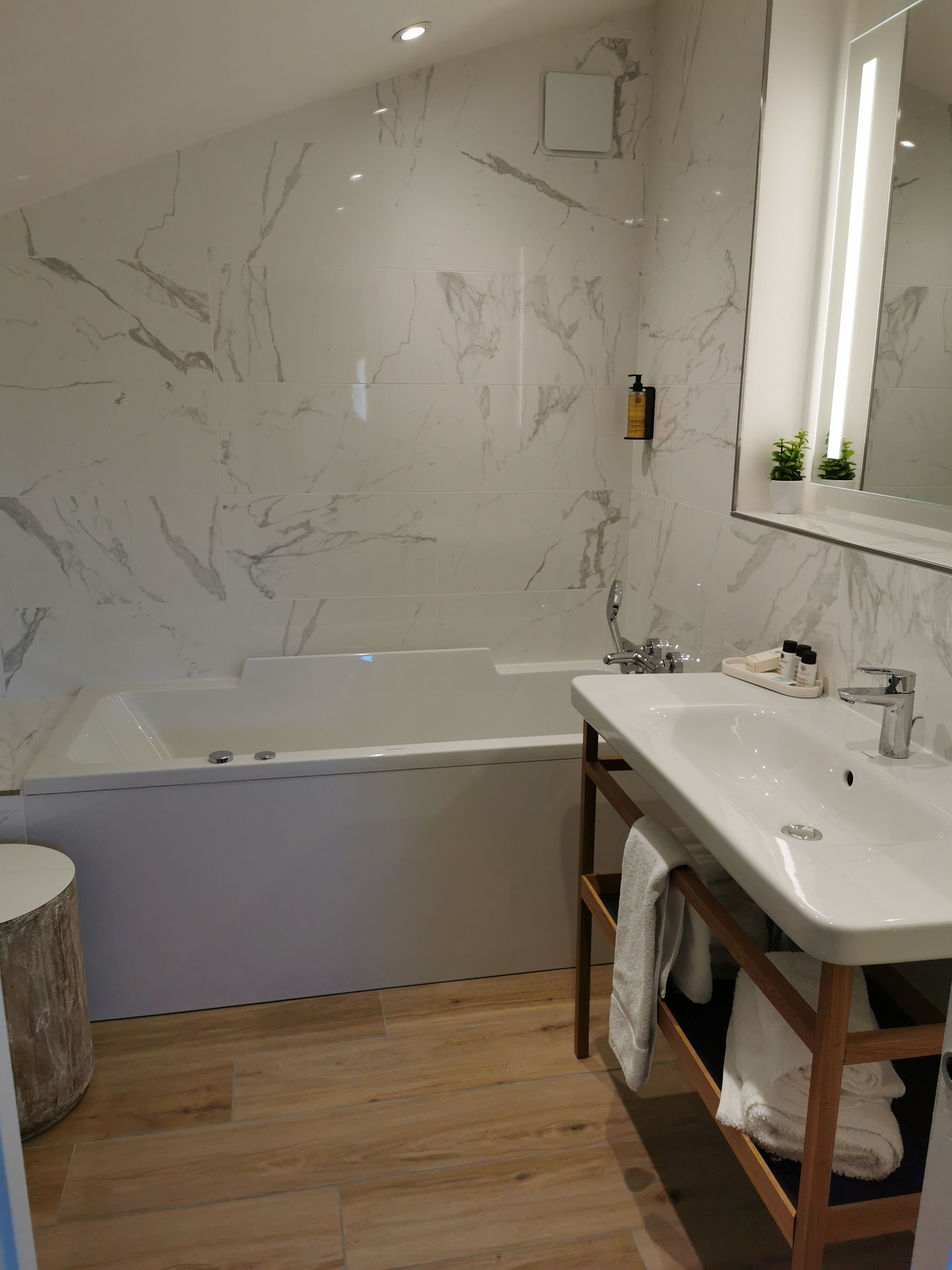 A modern bathroom with a marble wall, a bathtub, a sink, and a wooden vanity.