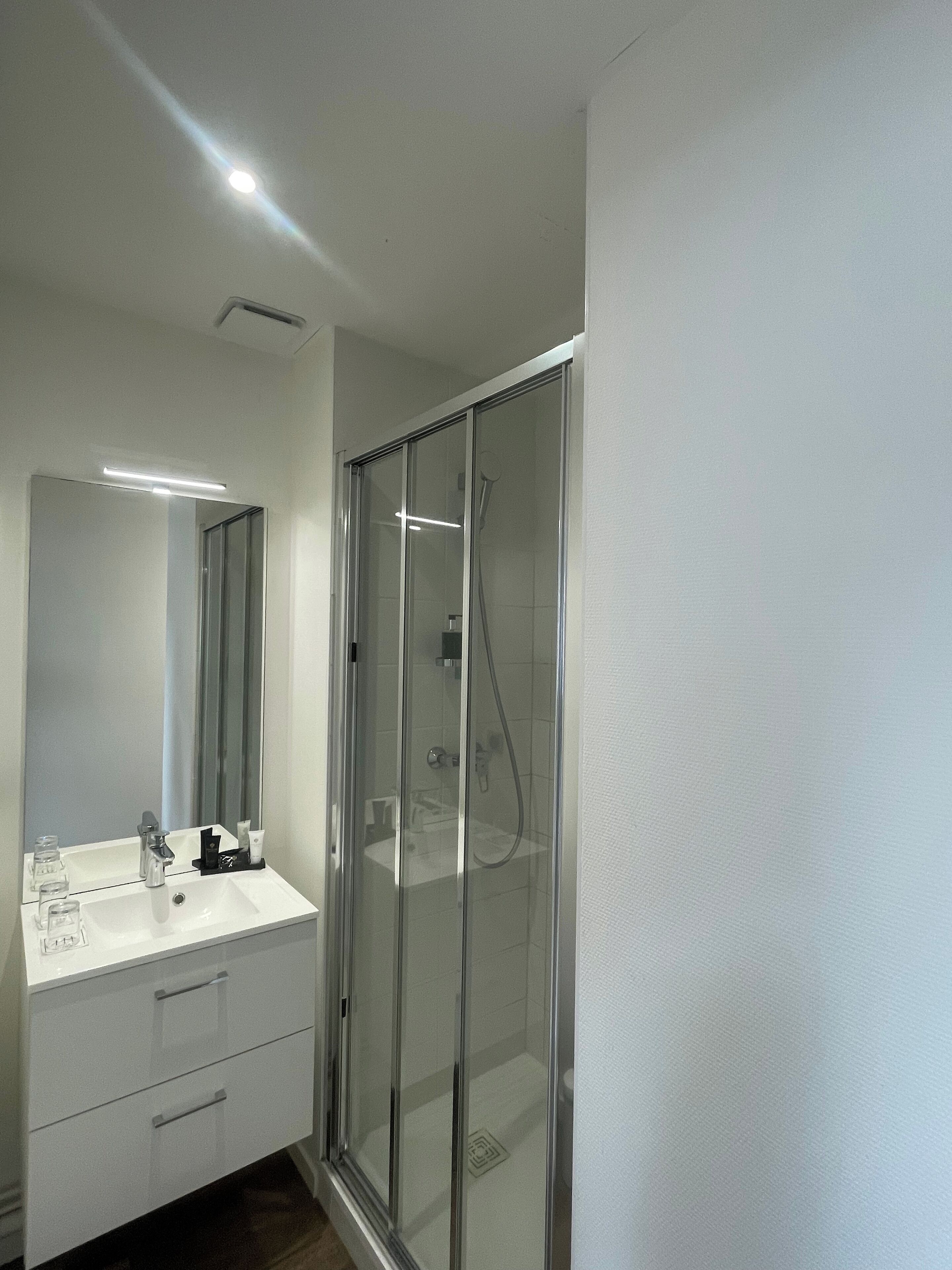 A modern bathroom with a glass-enclosed shower, a white sink with a mirror, and a small cabinet.