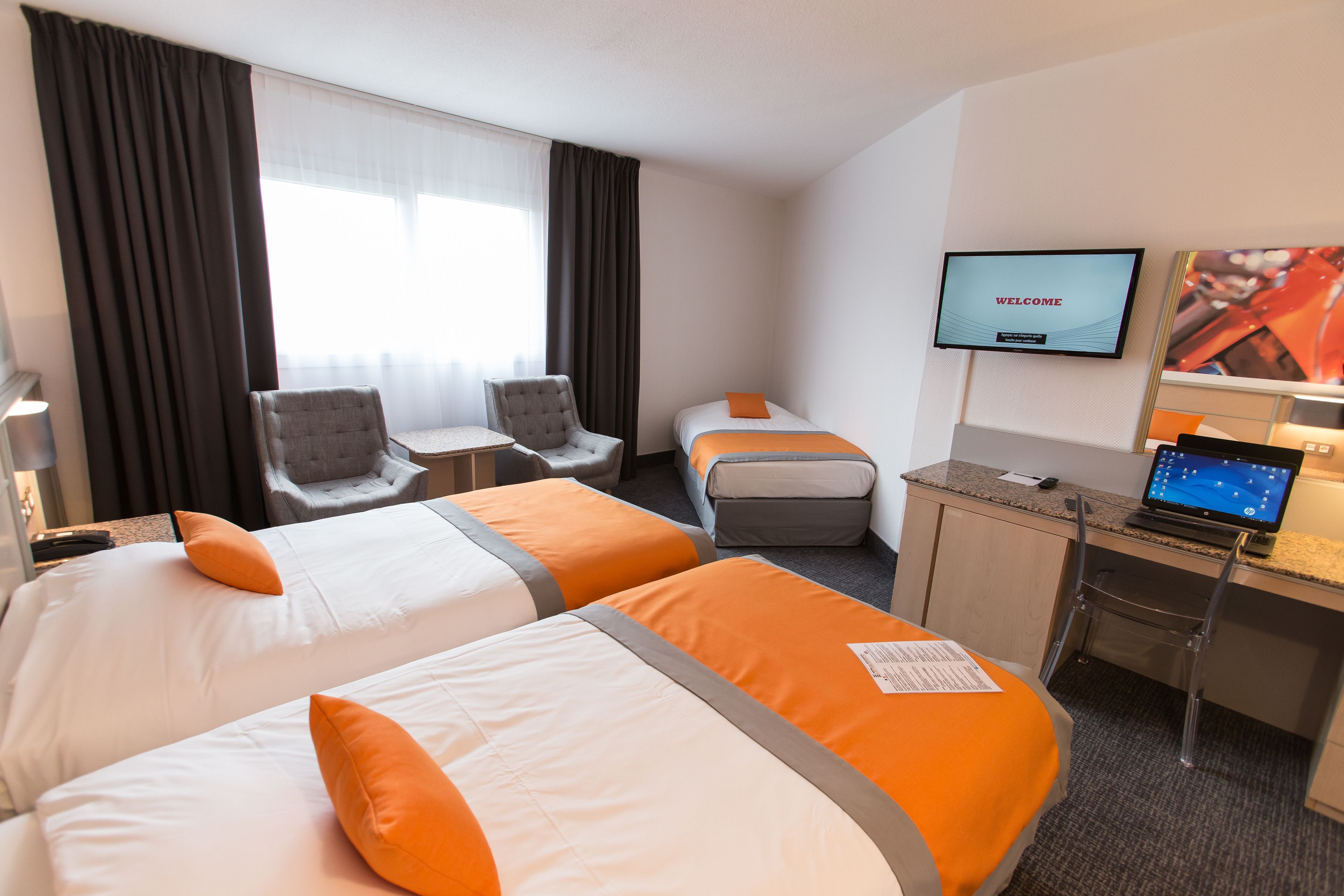Une chambre d’hôtel avec deux lits, un bureau avec un ordinateur portable, une télévision et une chaise.