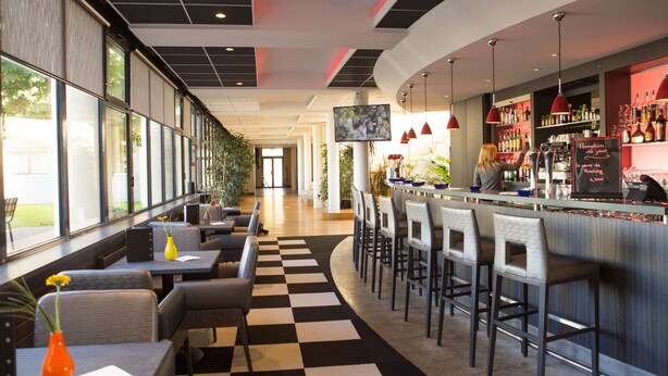A modern bar area with seating, a television screen, and a bar stocked with bottles.