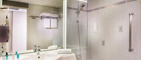 Un baño moderno con ducha de vidrio, lavamanos con artículos de aseo y un espejo.