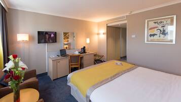 Habitación de hotel con cama, escritorio, silla, televisor y un jarrón con flores.