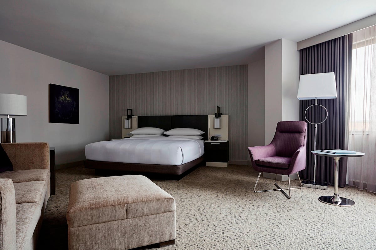 A hotel room with a large bed, a chair, a small table, and a lamp.