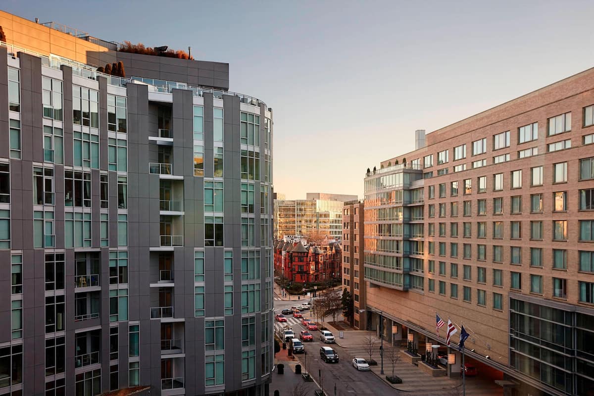 A modern hotel with a glass facade, multiple floors, and a parking area with cars.