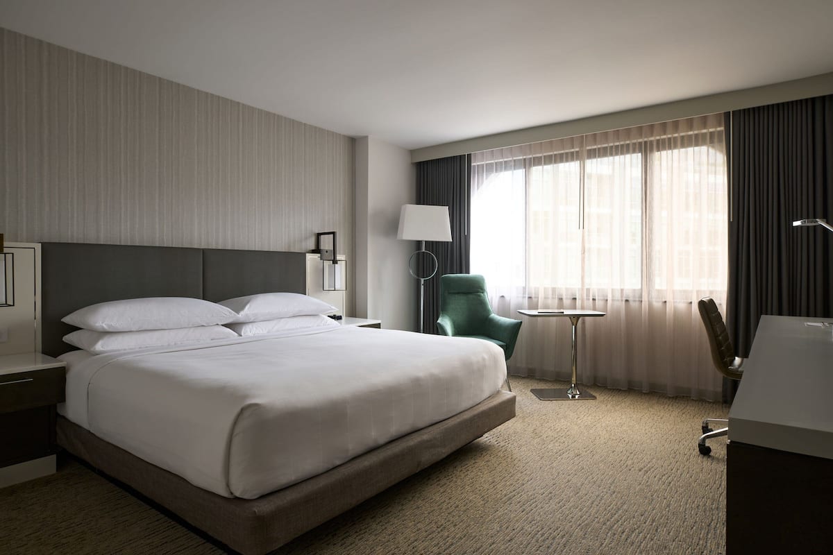 A hotel room with a large bed, a desk, a chair, and a window with curtains.
