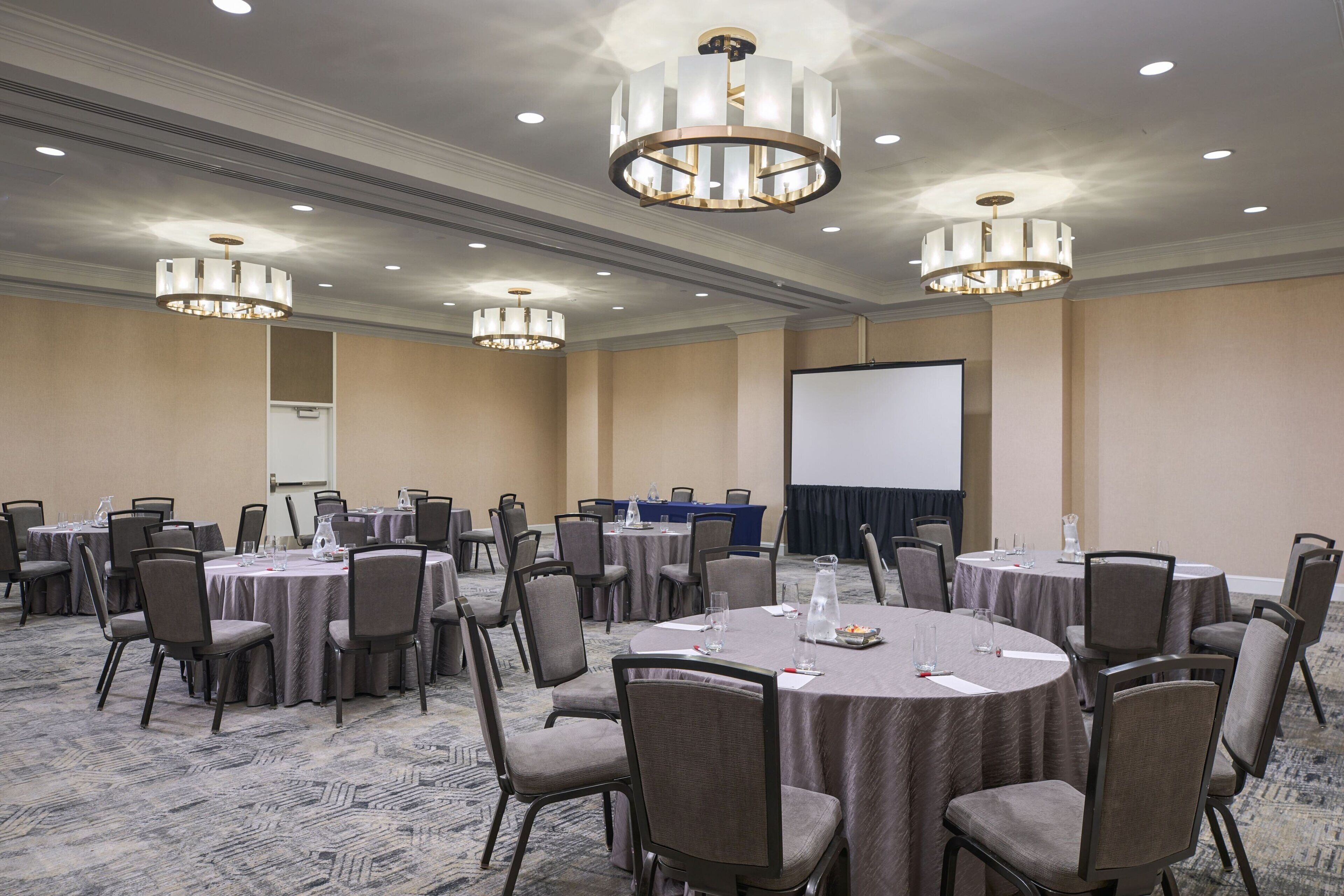 A conference room with round tables, chairs, and a projector screen.