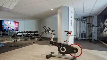 Uma academia moderna com equipamentos de cardio, máquinas de peso e uma televisão exibindo conteúdo de fitness.