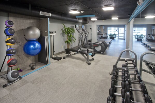 A gym with exercise equipment, treadmills, and a mirror wall.