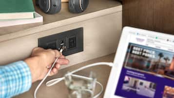 A person plugging in a device into a power outlet on a wooden desk with a laptop displaying a webpage.
