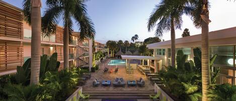 Un patio de hotel con piscina, mobiliario exterior y palmeras.