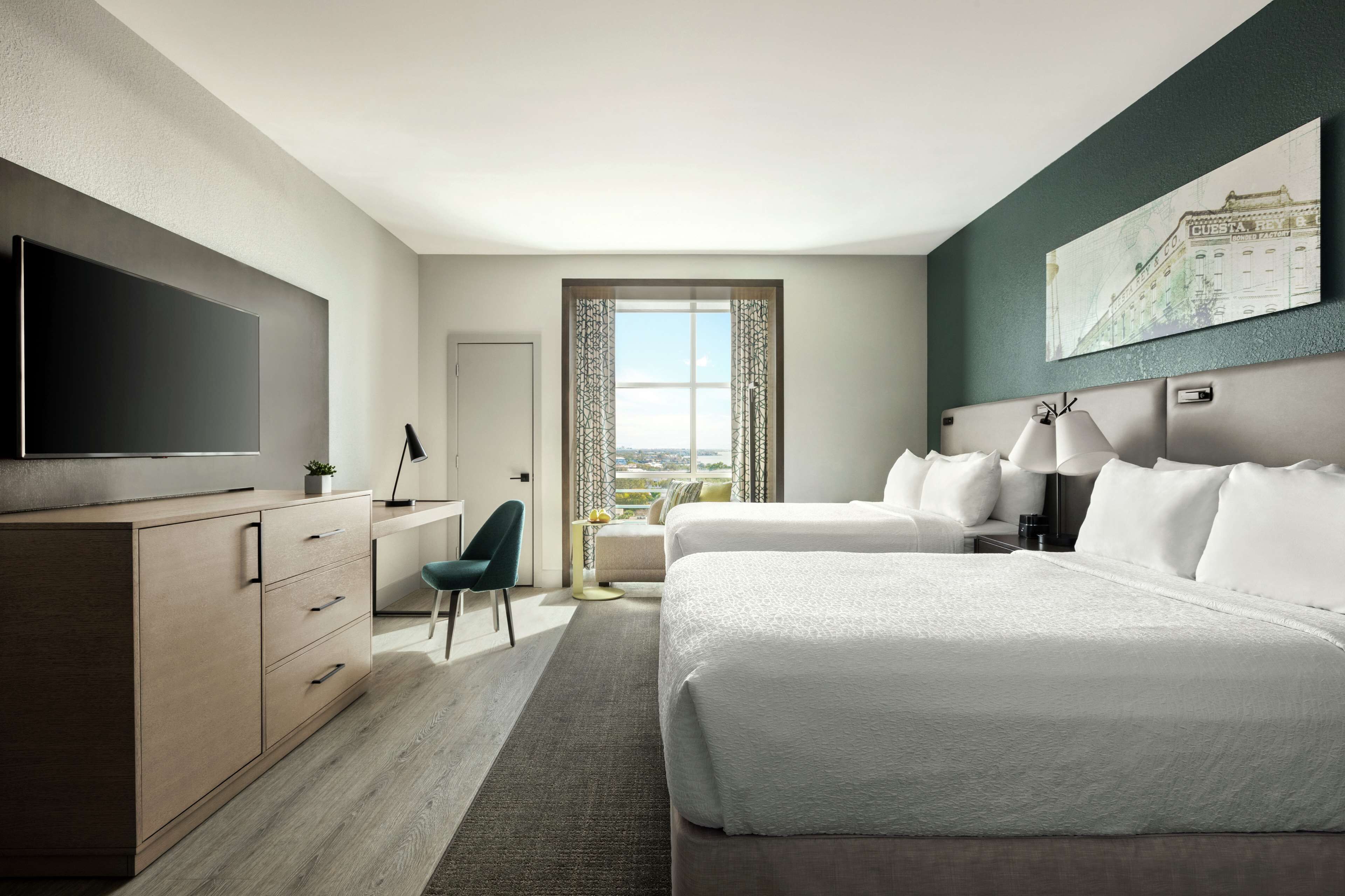Ein Hotelzimmer mit einem großen Bett, einem Schreibtisch mit Stuhl, einem Fernseher und einem Fenster mit Vorhängen.