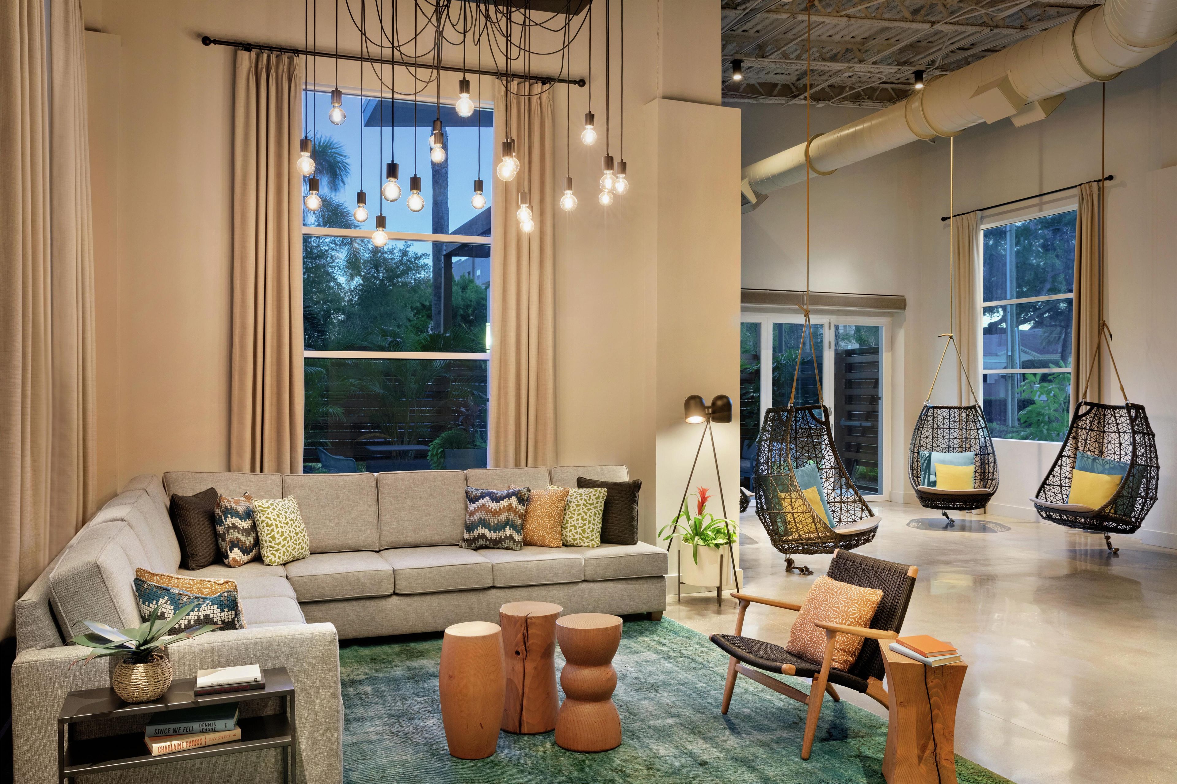 A modern living room with a sofa, coffee table, hanging chairs, and a large window with curtains.