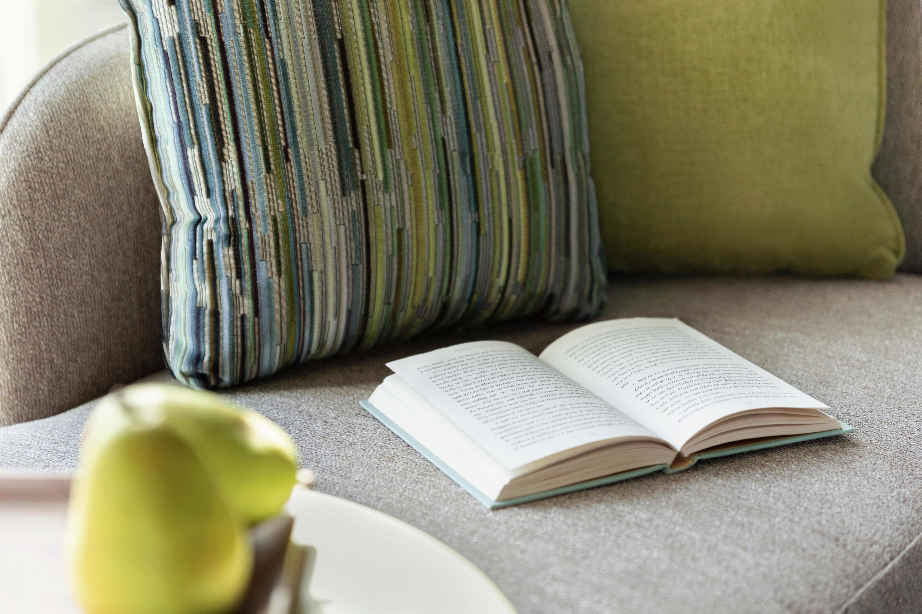 Un libro abierto sobre un sofá, con un cojín y una almohada al fondo.