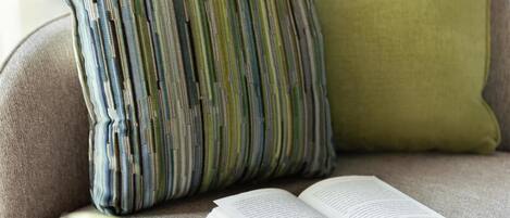Un libro abierto sobre un sofá, con un cojín y una almohada al fondo.