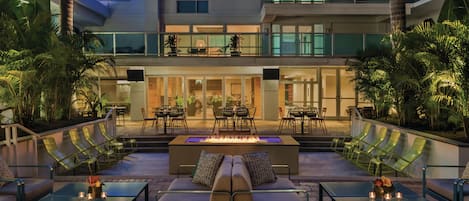 An outdoor seating area with a fire feature, lounge chairs, and a view of the building's interior.