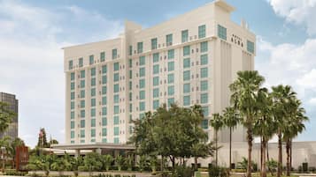 A multi-story hotel with a modern design, featuring a prominent entrance and a landscaped front yard with palm trees.