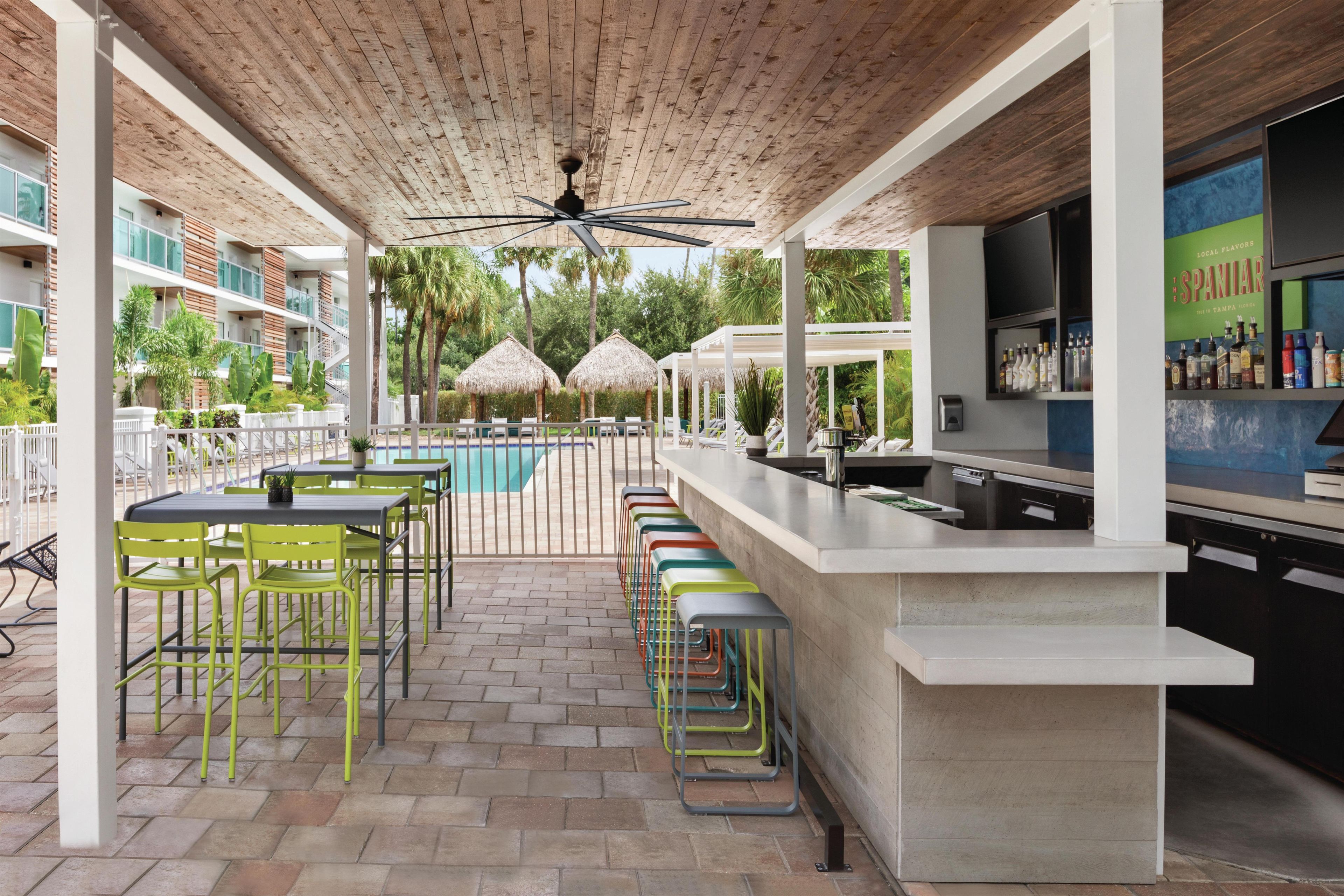 A covered outdoor bar area with a pool, seating, and a bar counter.
