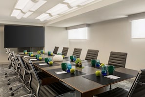 A conference room with a long table, chairs, a projector screen, and decorative items.
