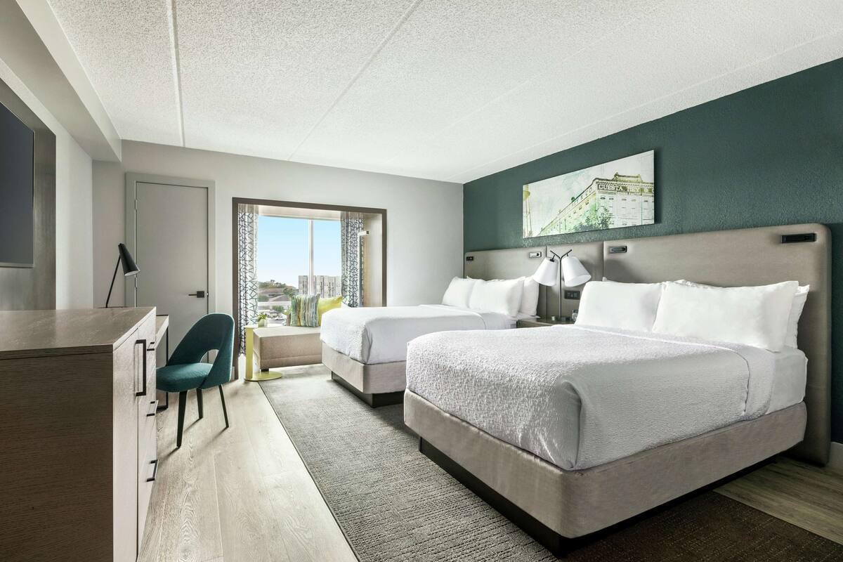 Ett hotellrum med två sängar, ett skrivbord, en stol och ett fönster med utsikt.