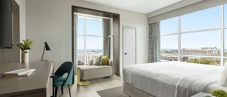 Une chambre d’hôtel moderne dotée d’un grand lit, d’un bureau, d’une chaise et offrant une vue sur la ville grâce à de grandes fenêtres.
