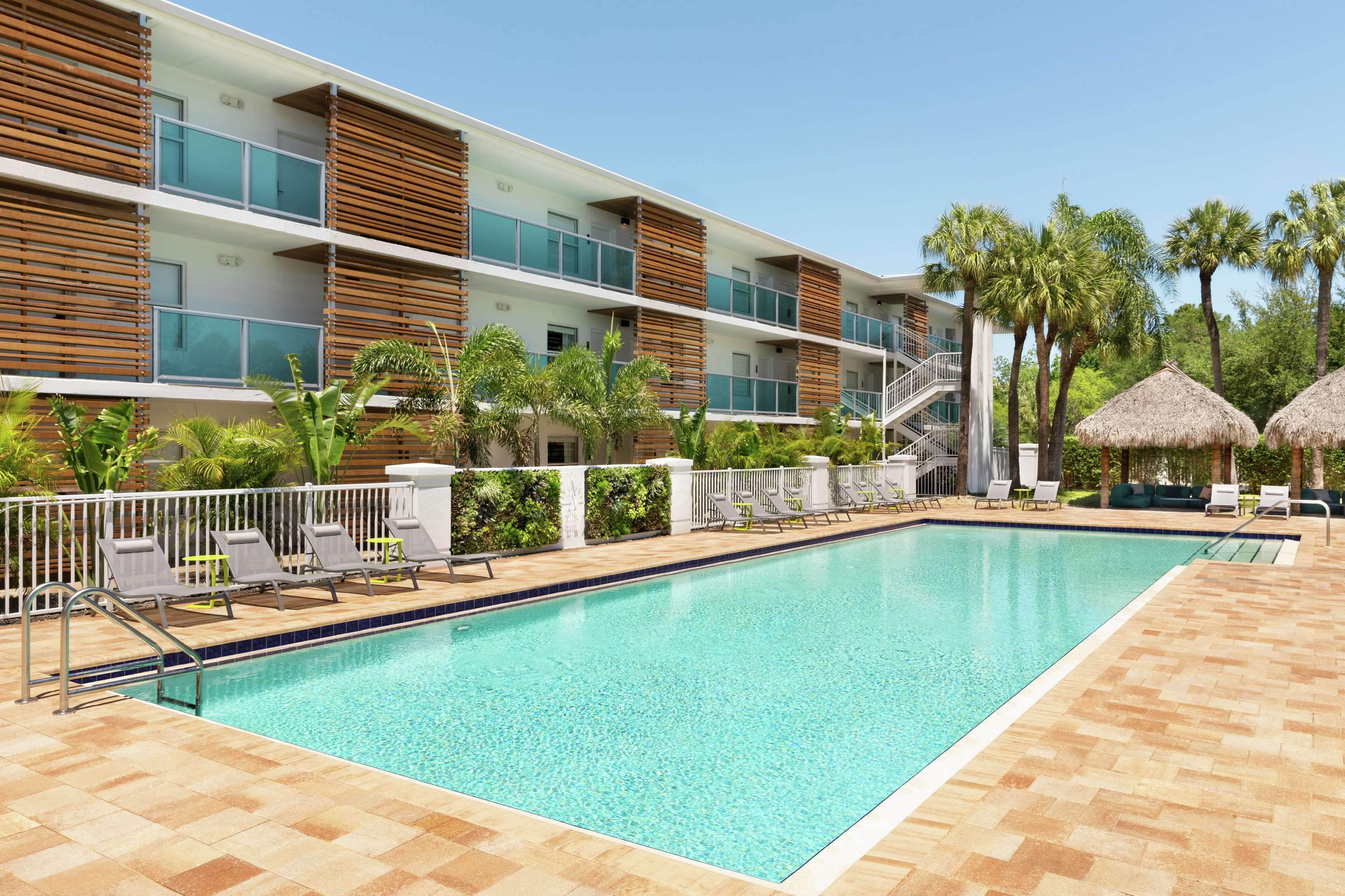 A modern hotel with a swimming pool, lounge chairs, and palm trees.