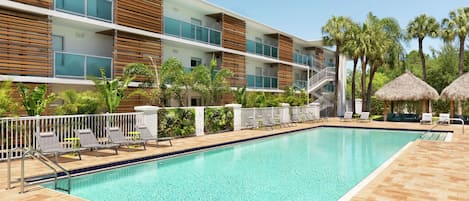 A modern hotel with a swimming pool, lounge chairs, and palm trees.